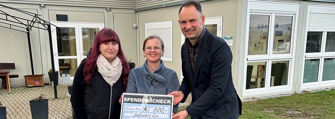 &Uuml;bergabe eines symbolischen Spendenschecks durch Andreas Peter und Nancy Schneider vom Autohaus Peter an Tierheimleiterin Jennifer Schenk (mit einem Dackel an der Leine) vor dem Tierheimgeb&auml;ude.