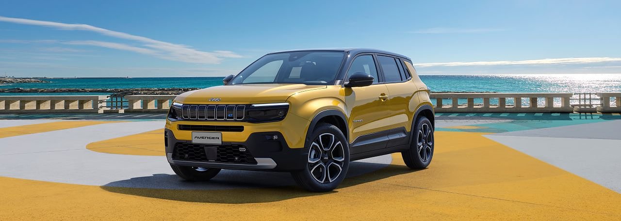 Gelber Jeep Avenger steht auf bunter Fläche direkt am Meer, mit blauem Himmel und Sonnenschein im Hintergrund.