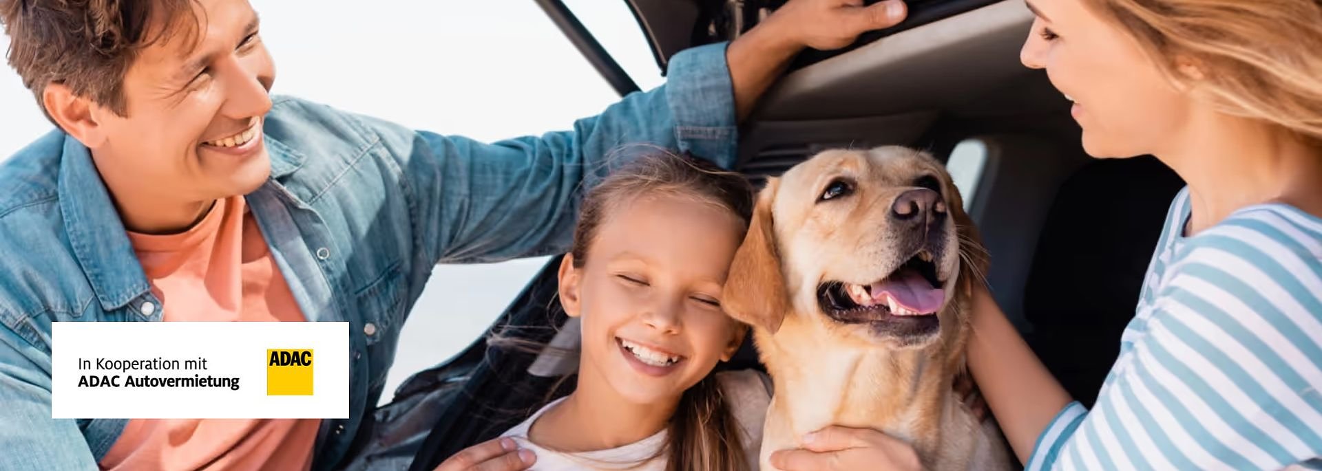 Glückliche Familie mit Kind und Hund sitzt im Auto, alle lächeln. Links unten ADAC-Logo mit Text „In Kooperation mit ADAC Autovermietung“.