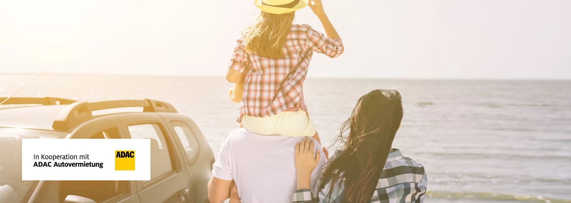 Familie am Strand: Mann trägt Kind auf den Schultern, Frau steht daneben, alle blicken aufs Meer; links unten ADAC-Logo mit Text „In Kooperation mit ADAC Autovermietung“.