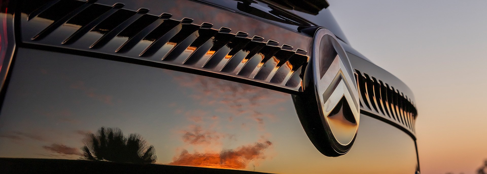 CITROËN-MODELLE - Nahaufnahme eines Citroën-Logos an einem glänzenden schwarzen Auto, mit Spiegelung eines Sonnenuntergangs und Palmen im Lack.