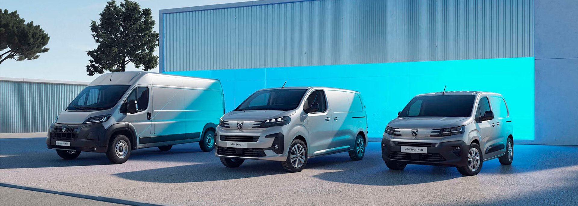 Drei Peugeot Transporter-Modelle stehen nebeneinander vor einer modernen Halle: links ein großer grauer Kastenwagen (Peugeot Boxer), in der Mitte ein silberner mittelgroßer Transporter (Peugeot Expert) und rechts ein kompakter grauer Lieferwagen (Peugeot Partner).
