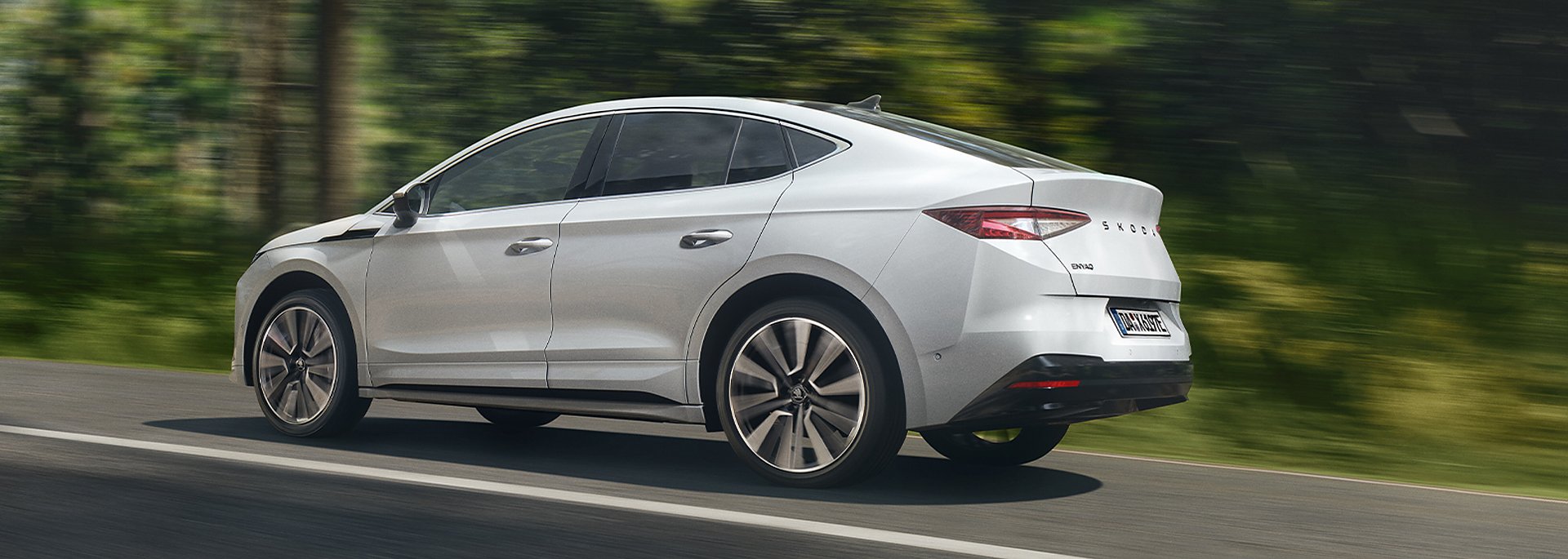 Skoda Enyaq Coupé in weiß fährt schnell auf einer Straße im Wald