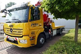 Gelber ADAC-Abschleppwagen mit Mercedes-Stern und der Aufschrift „Autohaus Peter“ an der Seite, geparkt neben einem Baum und Gebäuden, mit rotem Kranaufbau hinten. (Foto: Fischer/Autohaus Peter)