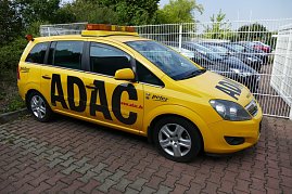 Gelber ADAC-Pannenhilfewagen vom Autohaus Peter, seitlich fotografiert auf einem gepflasterten Parkplatz, mit großem ADAC-Schriftzug und orangenem Warnlicht auf dem Dach. Im Hintergrund stehen weitere Fahrzeuge hinter einem weißen Zaun. (Foto: Fischer/Autohaus Peter)