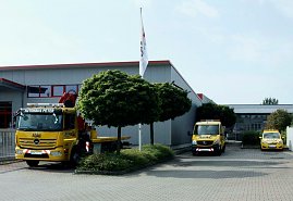 Drei gelbe ADAC-Fahrzeuge des Autohaus Peter, darunter ein Abschlepp-LKW, ein Transporter und ein PKW, stehen vor einem grauen Gebäude mit roten Fensterrahmen. Davor stehen zwei Bäume und ein Fahnenmast mit Fahne. Der Himmel ist leicht bewölkt. (Foto: Fischer/Autohaus Peter)