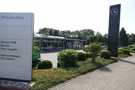 Außenansicht des Mercedes-Benz Autohauses Duderstadt mit großem Mercedes-Stern auf einer hohen Stele und einem Wegweiser, der auf Verkauf PKW, Service, Teile/Zubehör, Gebrauchtwagen sowie TÜV/DEKRA hinweist. Im Hintergrund ein modernes, verglastes Autohausgebäude, umgeben von gepflegten Grünflächen und Büschen. (Foto: Fischer/Autohaus Peter)