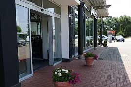  Eingangsbereich eines Autohauses der Peter Gruppe in Duderstadt, mit großen Glasfassaden, schwarzer Beschilderung und Blumen in Töpfen entlang des gepflasterten Weges; rechts stehen geparkte Autos, im Hintergrund Bäume und ein Parkplatz. (Foto: Fischer/Autohaus Peter)