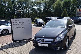 Parkplatz der Mercedes-Benz-Niederlassung in Duderstadt mit einem schwarzen Mercedes-Benz im Vordergrund. Daneben ein weißes Auto und ein Wegweiser mit Beschriftungen wie „Service“, „Teile/Zubehör“, „Verkauf PKW“ und „Gebrauchtwagen“. Im Hintergrund mehrere weitere Fahrzeuge und Bäume. (Foto: Fischer/Autohaus Peter)