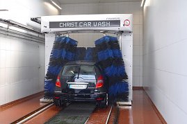 Auto in einer automatischen Waschanlage. Blaue und schwarze Bürsten reinigen das schwarze Fahrzeug. Die Umgebung ist hell und gekachelt, mit rutschfestem Boden. (Foto: Fischer/Autohaus Peter)