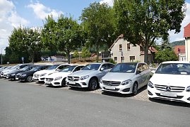 Reihe von Mercedes-Benz Gebrauchtwagen in verschiedenen Farben, geparkt auf einem Autohaus-Außenplatz. Im Hintergrund stehen Bäume, ein Wohnhaus mit rotem Dach und weitere Häuser, blauer Himmel mit einigen Wolken. (Foto: Fischer/Autohaus Peter)