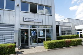 Eingangsbereich eines Autohauses mit Glasfront. Über der Tür hängt ein Schild mit der Aufschrift Annahme Transporter, Annahme LKW. Rechts ist eine Werkstatthalle mit großen Toren sichtbar, davor gepflegte Hecken und ein gepflasterter Weg. (Foto: Fischer/Autohaus Peter)