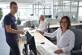 Freundlicher Empfangsbereich im Mercedes-Autohaus: Zwei Mitarbeiterinnen in weißer Kleidung sitzen hinter dem Tresen. Eine von ihnen berät einen jungen Kunden vor dem Tresen, während die Kollegin im Hintergrund telefoniert. (Foto: Fischer/Autohaus Peter)
