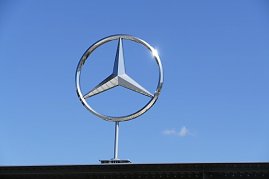 Großes silbernes Mercedes-Benz-Logo in Form des dreizackigen Sterns, montiert über einem Gebäudedach. Strahlend blauer Himmel im Hintergrund, die Sonne spiegelt sich am Rand des Logos. (Foto: Fischer/Autohaus Peter)