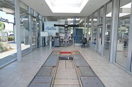 Helles, modernes Mercedes-Benz-Autohauses mit großen Glasfronten. In der Mitte eine Fahrzeughebebühne im Boden eingelassen, dahinter Werkstattausrüstung und ein Schreibtisch mit Stuhl. Rechts Glasbüros mit Blick in den Innenraum. (Foto: Fischer/Autohaus Peter)