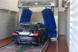 Ein schwarzer Mercedes-Benz wird in einer automatischen Waschanlage mit blauen Bürsten gereinigt. Das Fahrzeug ist mit Schaum bedeckt, die Anlage befindet sich in einer gefliesten Halle. (Foto: Fischer/Autohaus Peter)
