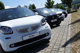 Nahaufnahme einer Reihe von Smart-Autos in Weiß und Schwarz, schräg geparkt auf einem gepflasterten Parkplatz vor dem Autohaus Peter in Northeim, sonniger Tag mit Bäumen und Hügeln im Hintergrund. (Foto: Fischer/Autohaus Peter)