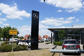 Mercedes-Autohaus mit großer Glasfassade und Mercedes-Stern aus Buschwerk. Links ein gelbes Ortsschild mit der Aufschrift Petershütte Stadt Osterode am Harz. Mehrere geparkte Autos, blauer Himmel mit weißen Wolken. (Foto: Fischer/Autohaus Peter)