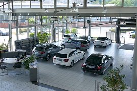 Großer, heller Showroom des Autohauses mit großen Glasfronten. Mehrere Mercedes-Benz Fahrzeuge in verschiedenen Farben (schwarz, silber, weiß) stehen ausgestellt. Links Bürotische mit Pflanzen und Unterlagen. Draußen sind weitere Autos und Grünflächen sichtbar. Die Atmosphäre wirkt modern und einladend. (Foto: Fischer/Autohaus Peter)