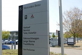 Großes Schild vor dem Mercedes-Benz Autohaus Peter in Dessau. Auf dem Schild stehen die Bereiche: Verkauf, Service, Teile/Zubehör, Gebrauchtwagen, Junge Sterne, TruckWorks und Van ProCenter. Oben Logos von Mercedes-Benz, Smart und Fuso. Im Hintergrund Glasfassade des Autohauses, parkende Autos und ein Baum. (Foto: Fischer/Autohaus Peter)