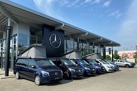 Außenansicht des Mercedes-Benz Autohauses in Dessau. Vor dem modernen Glasgebäude mit großem Mercedes-Stern-Logo stehen mehrere blaue und weiße Mercedes-Vans in einer Reihe. Drei Vans haben ausgeklappte Aufstelldächer. (Foto: Krüger/Peter-Autozentrum-Anhalt)