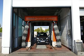 Ein grauer Smart fährt gerade in eine Autowaschanlage mit orangefarbener Beschriftung Christ CAR WASH. Links und rechts hängen graue Bürsten. (Foto: Fischer/Autohaus Peter)