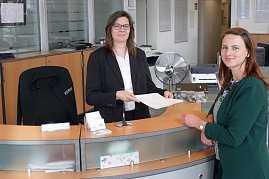 Zwei Frauen am Empfangstresen des Mercedes-Autohauses in Zerbst. Die Mitarbeiterin übergibt ein Dokument an die Kundin, beide lächeln in die Kamera. (Foto: Fischer/Autohaus Peter)