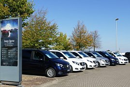 Reihe von weißen und dunklen Mercedes-Benz Vans mit Junge Sterne-Schildern auf dem Parkplatz des Autohauses, links ein großes Werbeschild, im Hintergrund Bäume und blauer Himmel. (Foto: Fischer/Autohaus Peter)