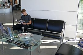 Kundenwartebereich im Mercedes-Benz Autohaus Bernburg, ein junger Mann sitzt auf einer schwarzen Ledersitzgruppe und liest eine Broschüre, davor ein Glastisch mit Zeitschriften. (Foto: Fischer/Autohaus Peter)