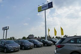 Autohaus-Außenbereich mit mehreren grauen Opel-Fahrzeugen in einer Reihe geparkt. Im Hintergrund ein hoher Mast mit einem Schild „Autohaus Peter Gruppe“ und Peugeot-Logo sowie gelbe Fahnen mit Opel-Logo.  (Foto: Fischer/Autohaus Peter)