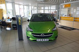Heller Verkaufsraum des Opel-Autohauses mit einem grünen Opel Corsa im Vordergrund. Links stehen Schreibtische mit Stühlen und Informationsmaterialien. Im Hintergrund sieht man den Empfangsbereich, an der eine Mitarbeiterin sitzt. Große Fenster lassen viel Tageslicht herein, und die Decke ist mit weißen Paneelen versehen. Ein Schild mit der Aufschrift "CORSA" steht neben dem Auto. (Foto: Fischer/Autohaus Peter)