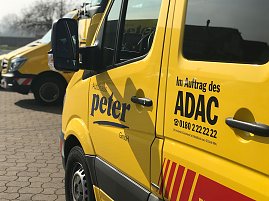 Gelber ADAC-Transporter vom Autohaus Peter, Nahaufnahme der Seitentür mit den Logos „Autohaus Peter“ und „Im Auftrag des ADAC“ sowie Telefonnummer. Im Hintergrund weitere gelbe ADAC-Fahrzeuge, gepflasterter Hof und Bäume. (Foto: Autohaus Peter GmbH )