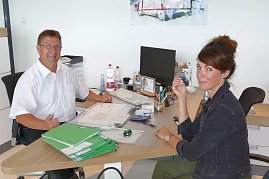 Beratungsgespräch im Skoda-Autohaus: Ein Mitarbeiter in weißem Hemd sitzt an einem Schreibtisch mit einer Kundin, beide lächeln freundlich in die Kamera. (Foto: Fischer/Autohaus Peter)