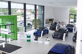 Heller koda-Showroom mit großen Fensterfronten, mehreren ausgestellten Fahrzeugen, einem markanten grünen Eingangselement und Zubehör auf weißen Podesten. (Foto: Fischer/Autohaus Peter)
