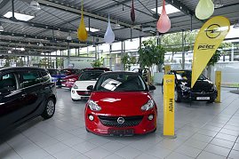 Innenansicht eines Autohauses mit mehreren ausgestellten Opel-Fahrzeugen, darunter ein roter Opel Adam im Vordergrund und ein schwarzer Opel Corsa im Hintergrund; gelbe Opel-Werbeflaggen und bunte Dekoelemente hängen von der Decke. (Foto: Fischer/Autohaus Peter)