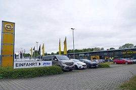 Außenansicht des Opel-Autohauses Peter in Göttingen mit moderner Glasfassade, gelbem Opel-Logo, zahlreichen geparkten Autos und einem großen Einfahrt-Schild im Vordergrund. (Foto: Fischer/Autohaus Peter)