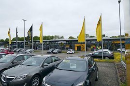 Opel-Autohaus Peter in Göttingen mit moderner Glasfassade, mehreren gelben Opel-Flaggen im Vordergrund und zahlreichen geparkten Fahrzeugen auf dem Außengelände. (Foto: Fischer/Autohaus Peter)