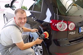 Pierre Heyer poliert die Heckseite eines schwarzen VW Golf Plus. Er trägt graue Arbeitskleidung, hält eine Poliermaschine in der Hand und schaut lächelnd in die Kamera. Das Fahrzeug glänzt stark, Spiegelungen sind deutlich zu sehen. (Foto: Fischer/Autohaus Peter)
