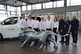 Gruppenfoto des Teams im Peugeot-Autohaus in Göttingen. Neun Mitarbeiterinnen und Mitarbeiter in weißer und schwarzer Kleidung stehen hinter einer großen grauen Löwenskulptur, links ein weißes Auto mit Peter-Logo. (Foto: Fischer/Autohaus Peter)