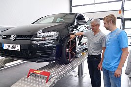 Schwarzer VW Golf GTD steht auf einer Hebebühne in einer Werkstatt. Ein Mitarbeiter in grauem Poloshirt zeigt einem Kunden in blauem T-Shirt Details am Rad. Beide lächeln und wirken im Gespräch vertieft. (Foto: Fischer/Autohaus Peter)