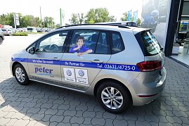 Silberner Volkswagen Golf Sportsvan mit großflächiger Werbebeschriftung der Autowelt Peter GmbH. Auf der Seite sind Logos von VW Service und VW Nutzfahrzeuge abgebildet. Das Fahrzeug steht auf gepflastertem Gelände vor einem Autohaus. (Foto: Fischer/Autohaus Peter)