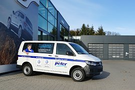 Ein weißer VW Transporter mit der Aufschrift Autowelt Peter GmbH steht vor einem modernen Autohaus mit großen Glasflächen. Auf dem Fahrzeug sind Logos für VW Service und VW Nutzfahrzeuge Service abgebildet sowie ein Bild einer Frau mit dem Text: Die beste Therapie für Langzeitbeziehungen. Eine Werkstatt, auf die man sich verlassen kann. (Foto: Fischer/Autohaus Peter)