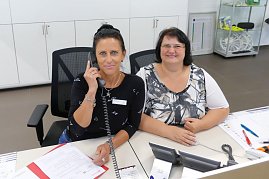 Zwei Mitarbeiterinnen an einem Empfangsschalter in einem Autohaus, eine Frau telefoniert und die andere lächelt in die Kamera. (Foto: Fischer/Autohaus Peter)