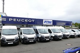 Reihe weißer Peugeot-Transporter vor einem Autohaus mit blauem Peugeot- und Autozentrum Peter-Logo. (Foto: Fischer/Autohaus Peter)