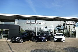 Glasfassade des Autohauses Peter mit der Aufschrift Gebrauchtwagen. Davor stehen drei Mercedes-Modelle: zwei schwarze SUVs und ein weißer Kombi, alle mit dem Schild Junge Sterne. Blauer Himmel, Spiegelungen von Bäumen und Umgebung in den Glasflächen. (Foto: Fischer/Autohaus Peter)