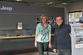 Christel Lauterbach und Danny Kindervater vom Jeep-Team stehen lächelnd vor dem Wartebereich im Jeep-Autohaus; im Hintergrund Wand mit Jeep-Logo und Felgen. (Foto: Fischer/Autohaus Peter)