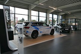Showroom eines modernen Jeep-Autohauses mit großen Fensterfronten, zwei ausgestellte Jeep-Modelle, eines mit künstlerischer blauer Folierung, das andere in Schwarz. (Foto: Fischer/Autohaus Peter)