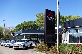 Mitsubishi-Center mit großer Glasfront und modernem schwarzen Design. Im Vordergrund stehen mehrere neue Fahrzeuge, daneben ein hohes schwarzes Schild mit Mitsubishi-Motors-Schriftzug, der Himmel ist blau. (Foto: Fischer/Autohaus Peter)