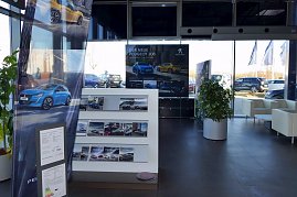 „Heller Ausstellungsbereich eines Autohauses mit Peugeot-Werbepostern, Prospektwand mit Flyern, Pflanze in großem Topf und Wartebereich mit weißen Sesseln, große Fenster mit Blick auf den Parkplatz. (Foto: Fischer/Autohaus Peter)