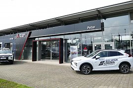 Eingangsbereich des Peter-Mehrmarkenhauses in Göttingen mit Mitsubishi-Logo, einem weißen Mitsubishi Eclipse Cross Plug-in Hybrid und einem weiteren Mitsubishi-Pickup vor dem Gebäude. (Foto: Fischer/Autohaus Peter)